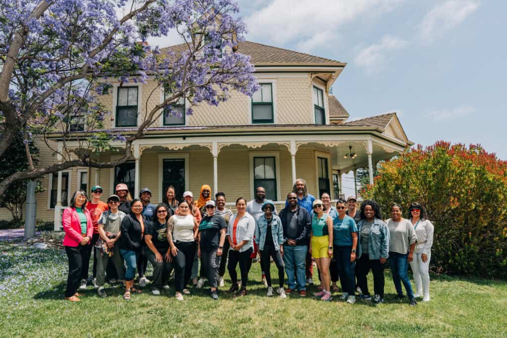 School of Political Leadership 2025 cohort members stand in front yard of a large, cream colored victorian home, posing and smiling.